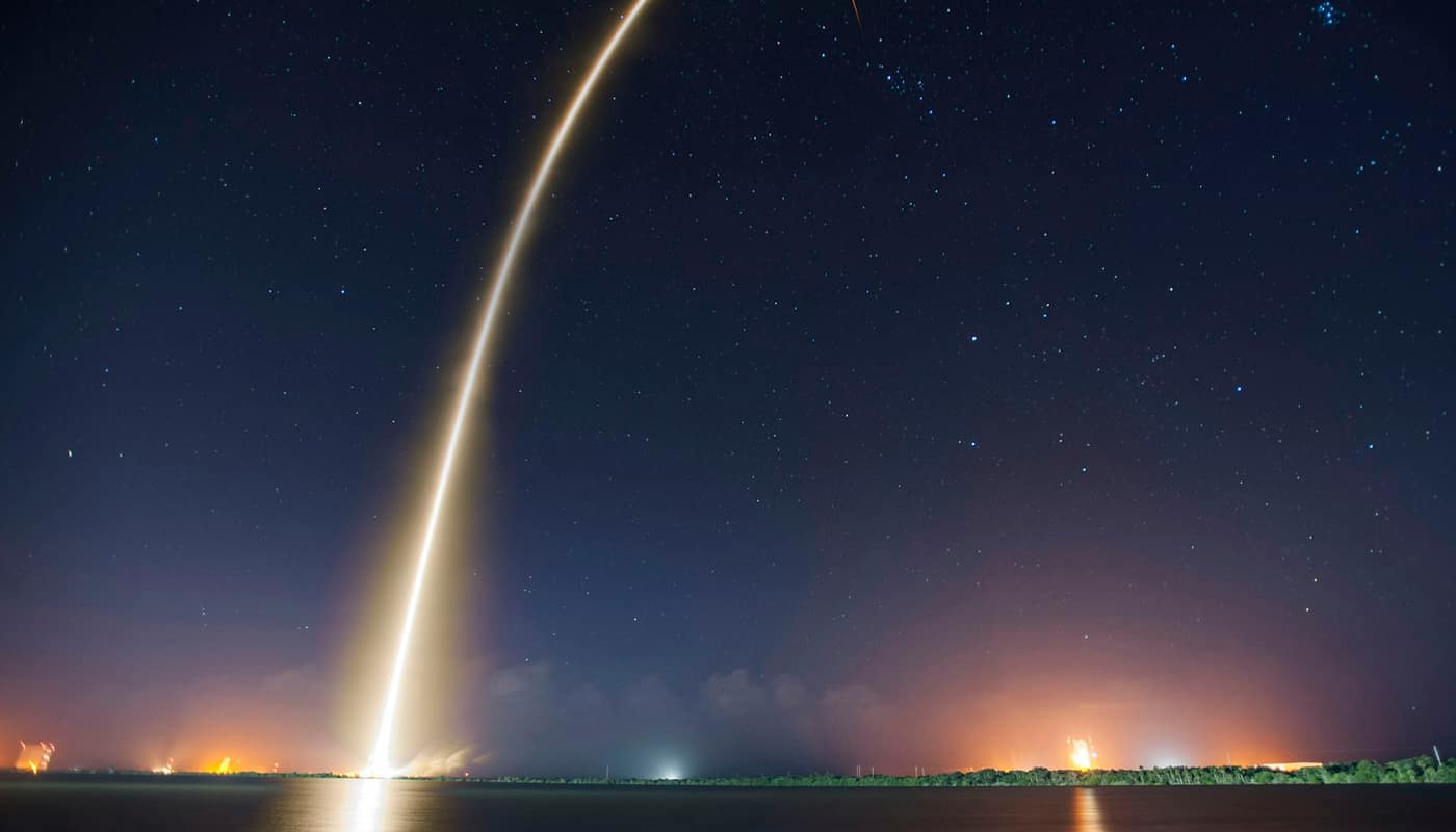 A rocket launch trail curving into a starry night sky