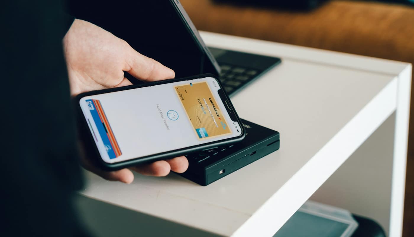 A hand holding a smartphone against a card reader for a contactless payment