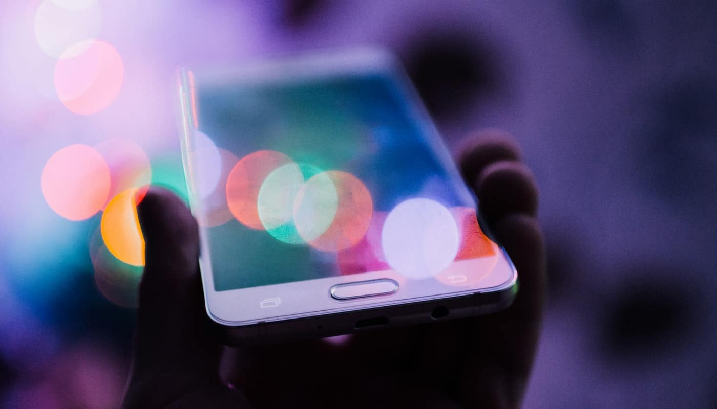 A smartphone held in a hand with colourful blurred lights